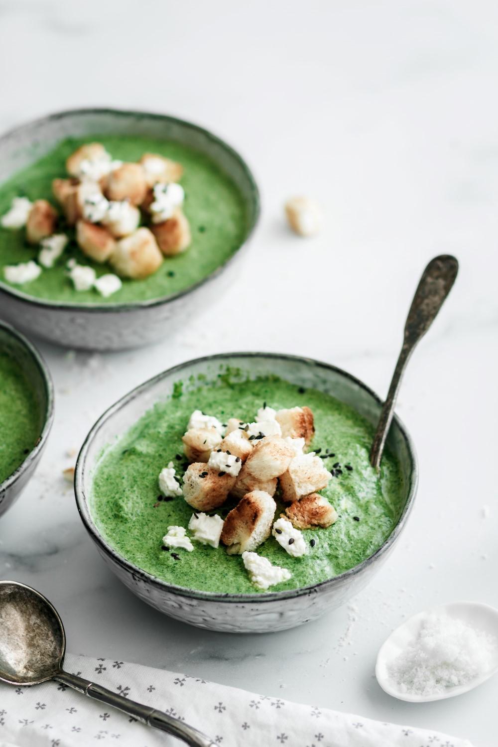 A bowl of green soup with bread cubes and cheese on top the article 5 best camera angles for food photography + which equipment to use by Anja Burgar