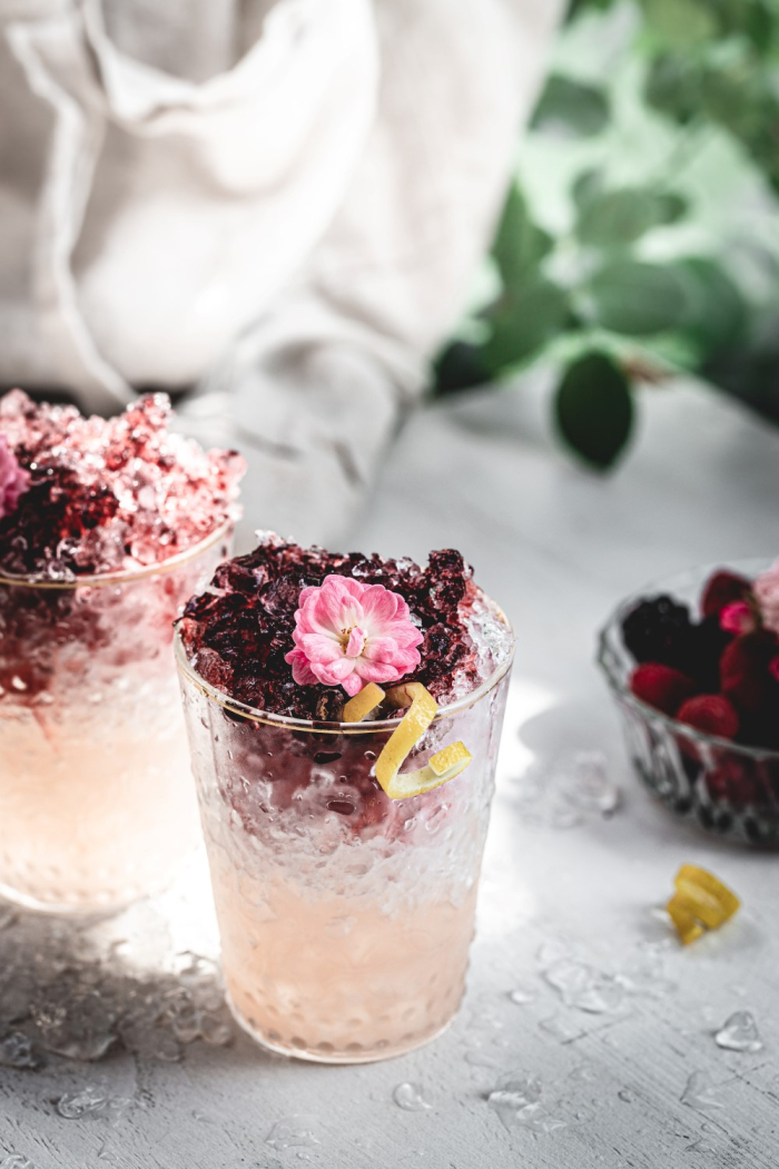 A purple and pink cocktail with crushed ice decorated with flowers